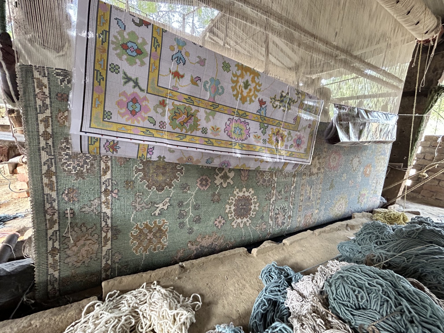 Oushak rug being hand-knotted on a traditional loom with its design reference