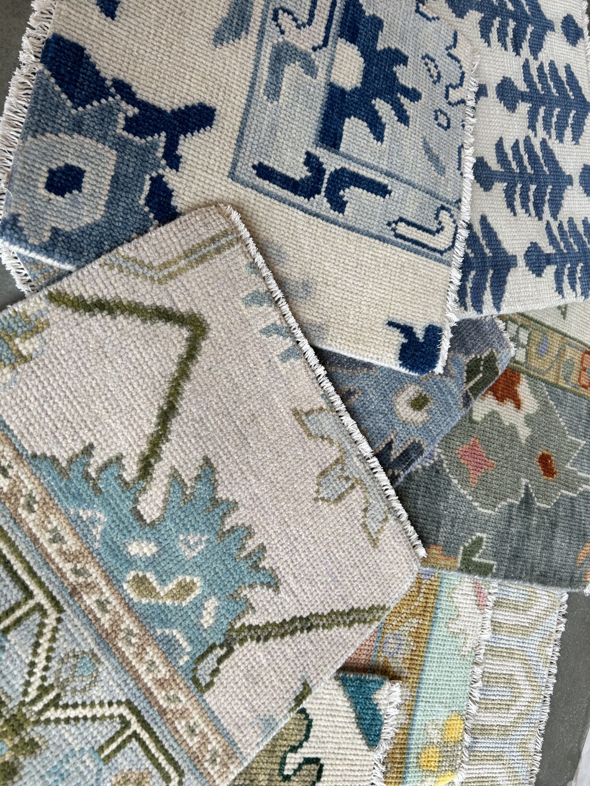 A layered library of hand-knotted rug samples in soft blue, ivory and green