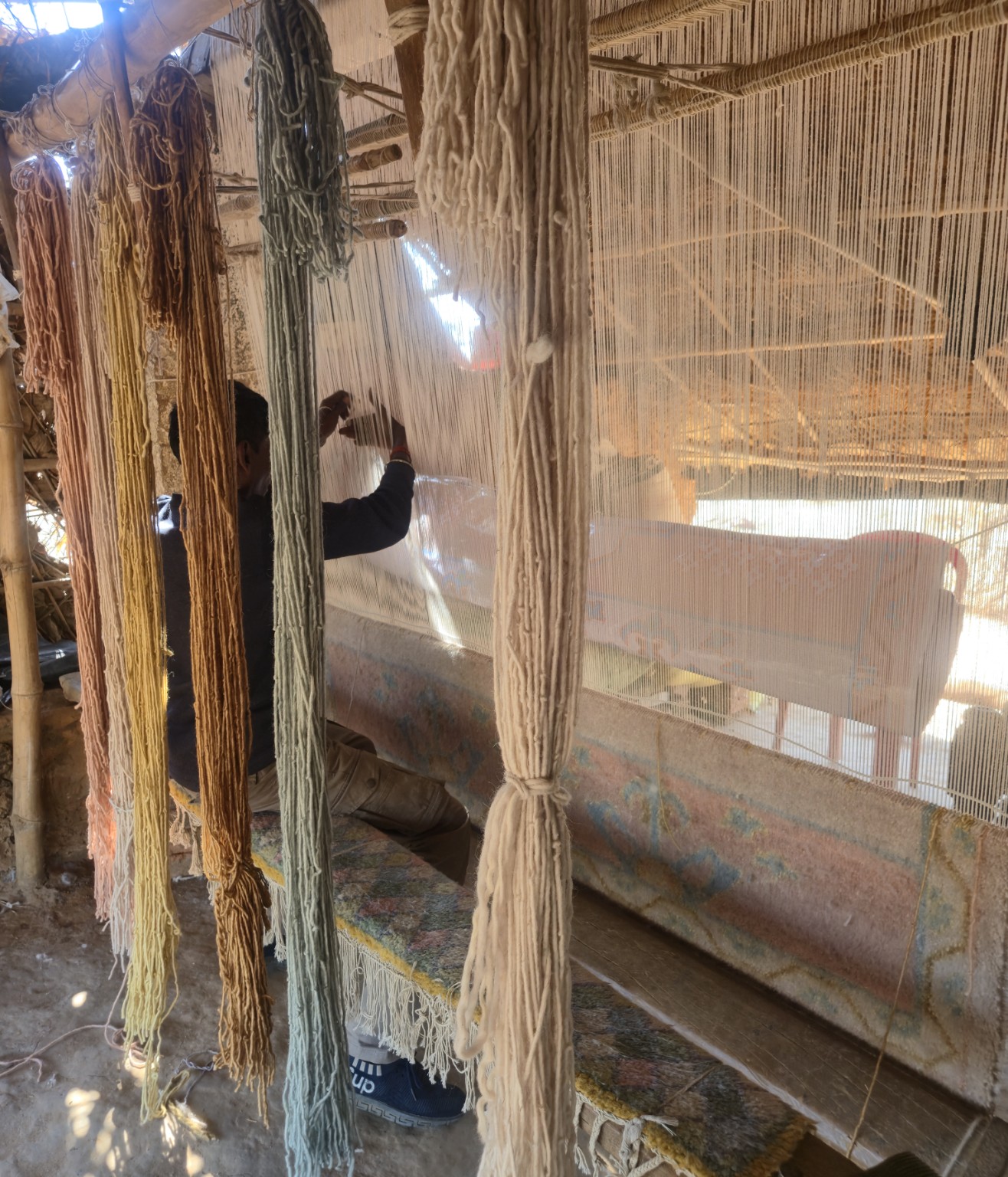An artisan working at a vertical rug loom, surrounded by hanging yarn.