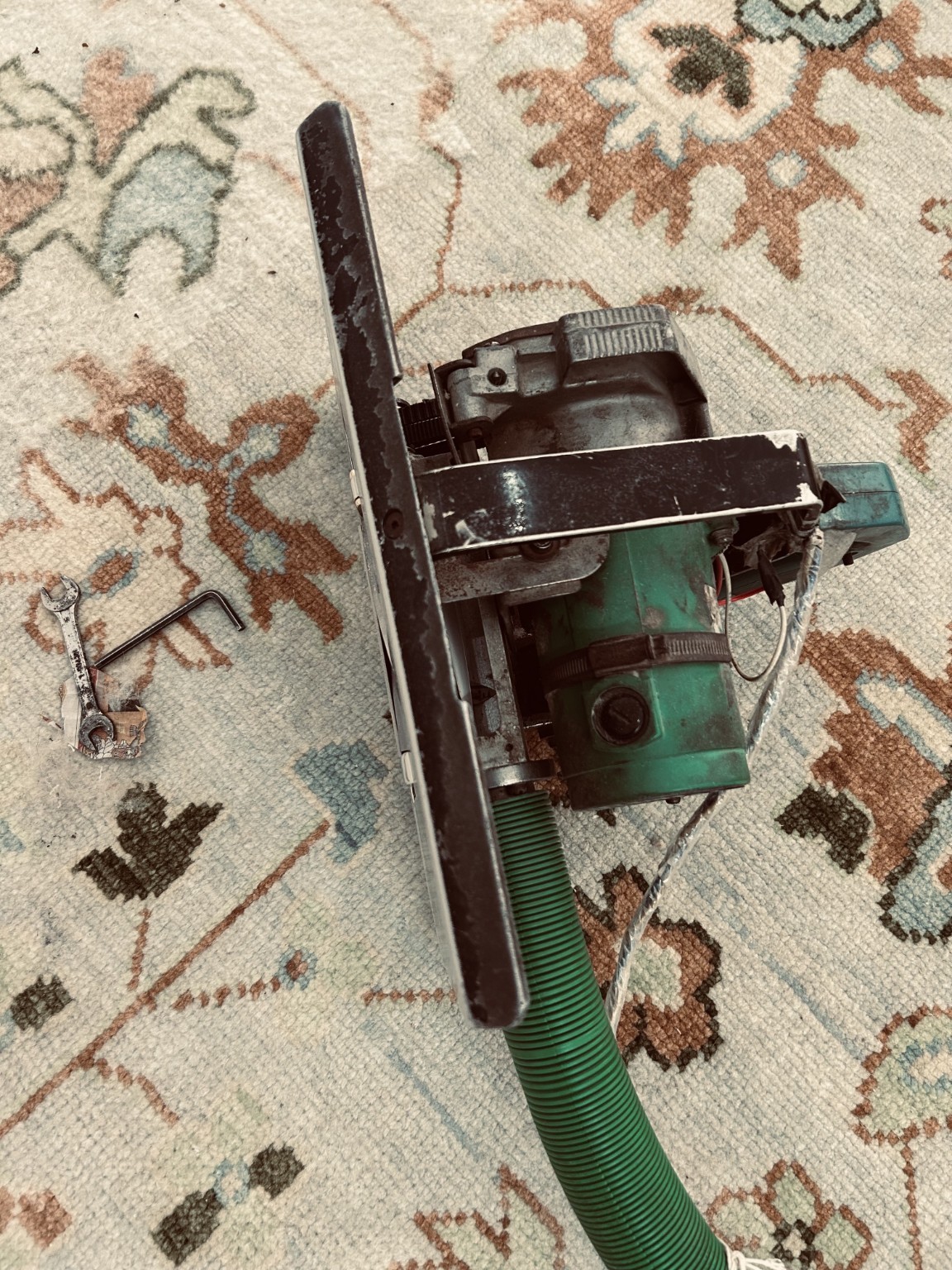 A rug-shearing machine and tools resting on a floral rug.