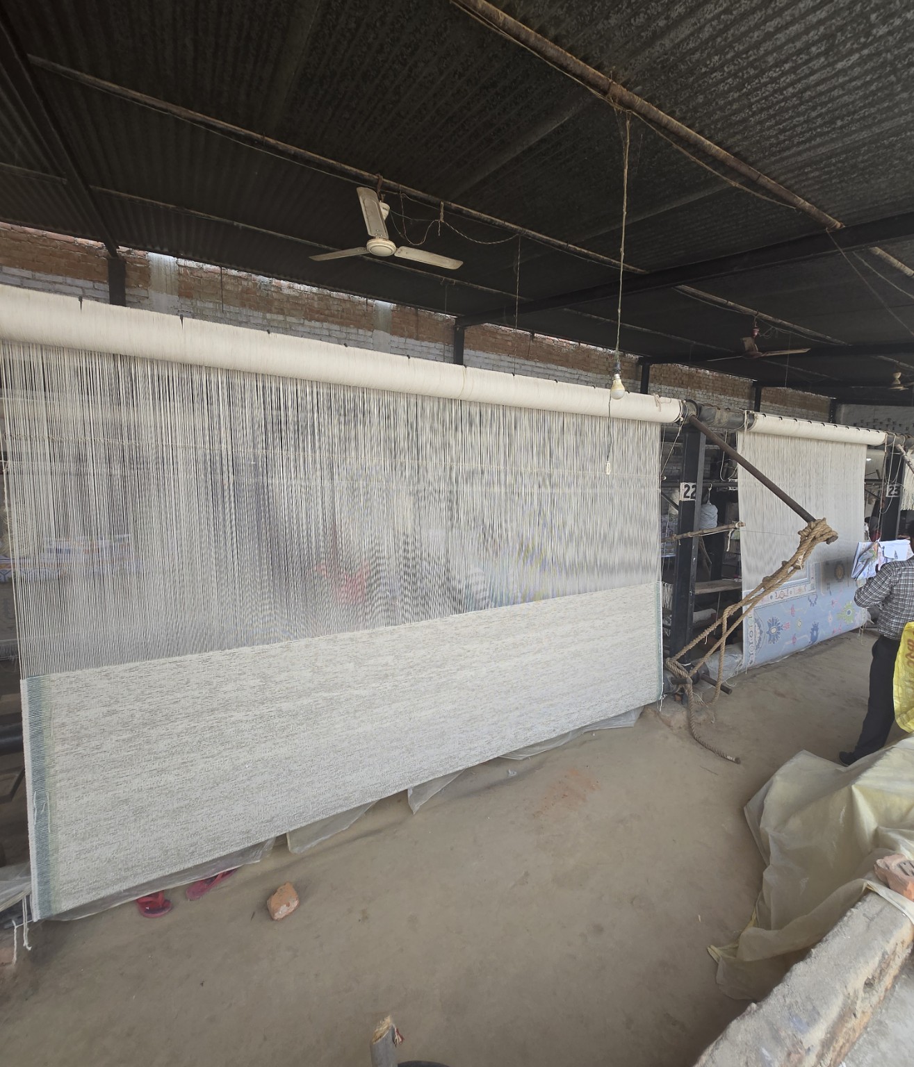 Vertical warp threads and rugs in progress on looms inside the workshop.